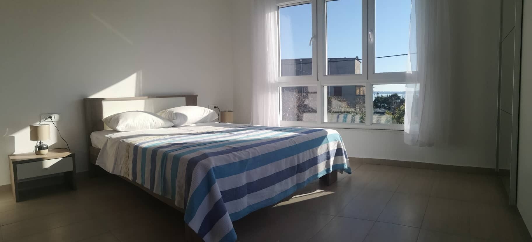 Un dormitorio con cama, mesita de noche, lámpara y ventana con cortinas.