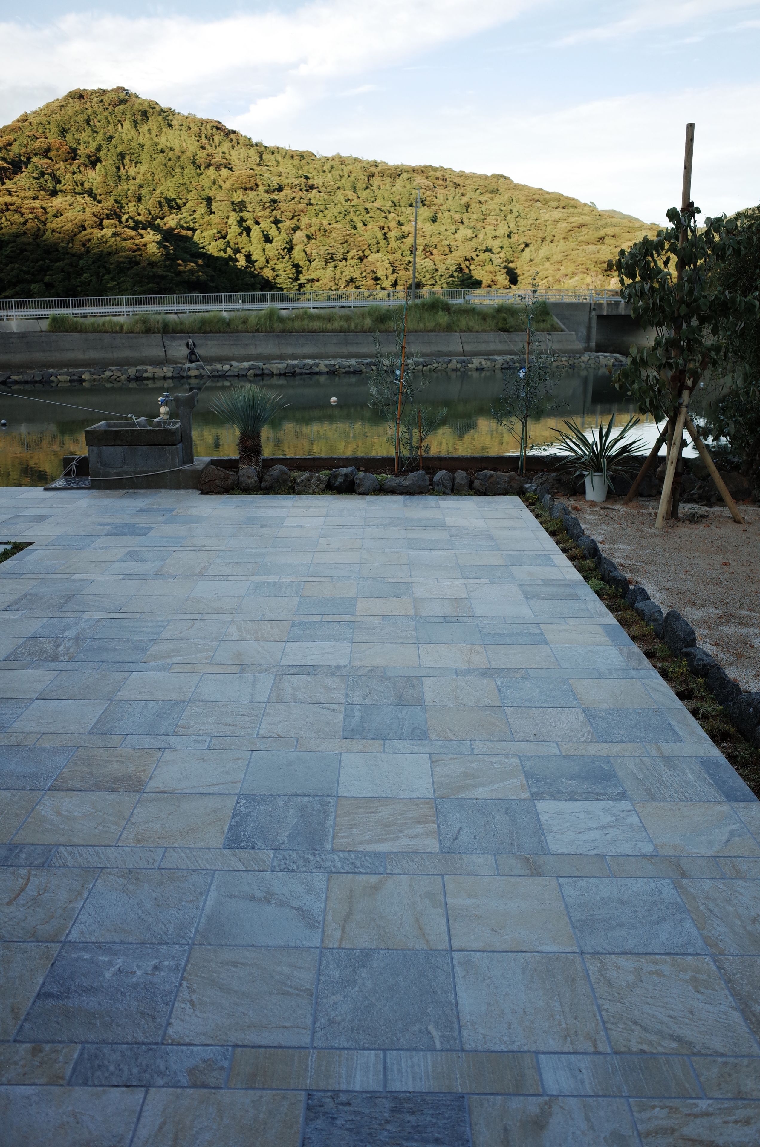 Un patio empedrado con vistas a un lago y una colina al fondo.