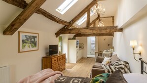A cozy bedroom with a sloped ceiling, wooden beams, a television, a cozy bed, and a view into the adjacent bathroom. - Secret Garden studio at Woodcock Farm (Bristol)