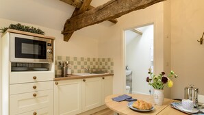 A kitchen with a microwave, sink, and wooden cabinets. There is a table with a plate of food and a vase of flowers. - Secret Garden studio at Woodcock Farm (Bristol)