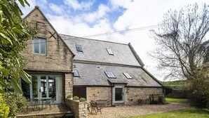A stone house with a sloped roof, a front porch with chairs, and a small garden area. - Secret Garden studio at Woodcock Farm (Bristol)