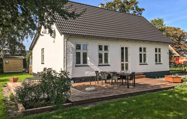 Enjoy a peaceful retreat in this charming home, featuring a front porch with a table and chairs, surrounded by a lush garden and well-manicured lawn.