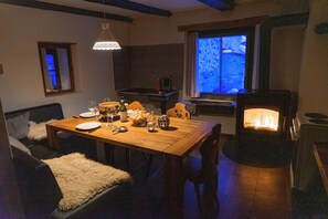 A cozy dining area with a wooden table set for two, a fireplace, and a window with a view. - Holiday house sunny and rustic, 2-8 P, in Val Poschiavo (Poschiavo)