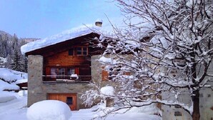 A rustic log cabin with a stone foundation, a balcony, and a snow-covered landscape.