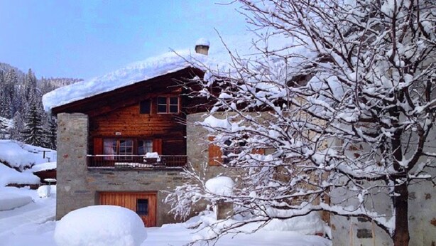 A rustic log cabin with a stone foundation, a balcony, and a snow-covered landscape. - Holiday house sunny and rustic, 2-8 P, in Val Poschiavo (Poschiavo)
