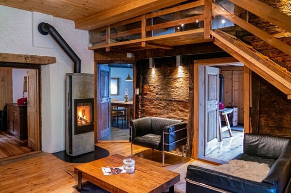 A cozy interior with a fireplace, wooden furniture, and a stone wall. - Holiday house sunny and rustic, 2-8 P, in Val Poschiavo (Poschiavo)