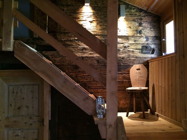 A wooden staircase with a lantern on the landing, a rustic wooden wall, and a wooden chair. - Holiday house sunny and rustic, 2-8 P, in Val Poschiavo (Poschiavo)