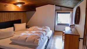 A bedroom with a wooden ceiling, a bed with white bedding, a wooden dresser, and a window with curtains. - Holiday house sunny and rustic, 2-8 P, in Val Poschiavo (Poschiavo)