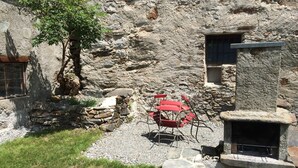 A rustic stone building with a small outdoor seating area featuring red chairs and a table. - Holiday house sunny and rustic, 2-8 P, in Val Poschiavo (Poschiavo)