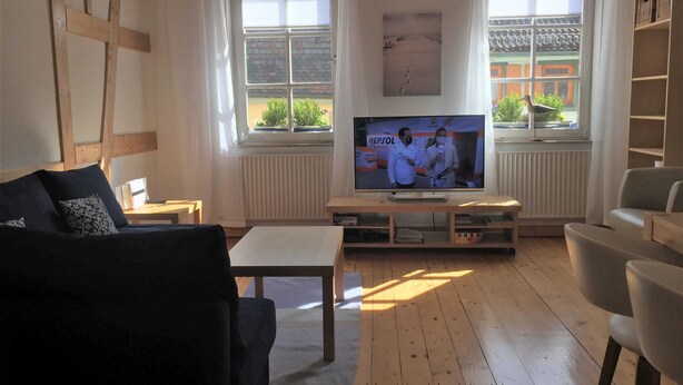 A living room with a television, wooden floor, and a view of a building outside. - Vacation apartment A, Salzgasse, Old Town - Edition Bad Wimpfen (Bad Wimpfen)