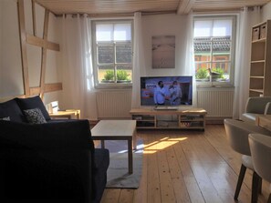 A living room with a television, wooden floor, and a view of a building outside. - Vacation apartment A, Salzgasse, Old Town - Edition Bad Wimpfen (Bad Wimpfen)