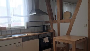 A kitchen with a wooden countertop, a stove, and a sink. There is a window with curtains, a wooden ceiling beam, and a small table with two chairs. - Vacation apartment A, Salzgasse, Old Town - Edition Bad Wimpfen (Bad Wimpfen)
