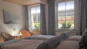 A hotel room with two beds, a chair, a table with a lamp, and a window with patterned curtains. - Vacation apartment A, Salzgasse, Old Town - Edition Bad Wimpfen (Bad Wimpfen)