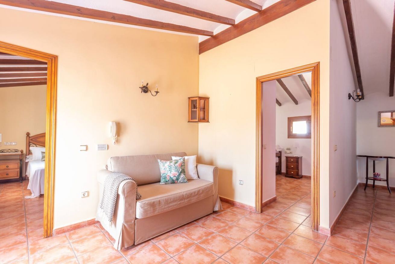 A cozy room with a sofa, a small cabinet, and a mirror. There is a door leading to another room.