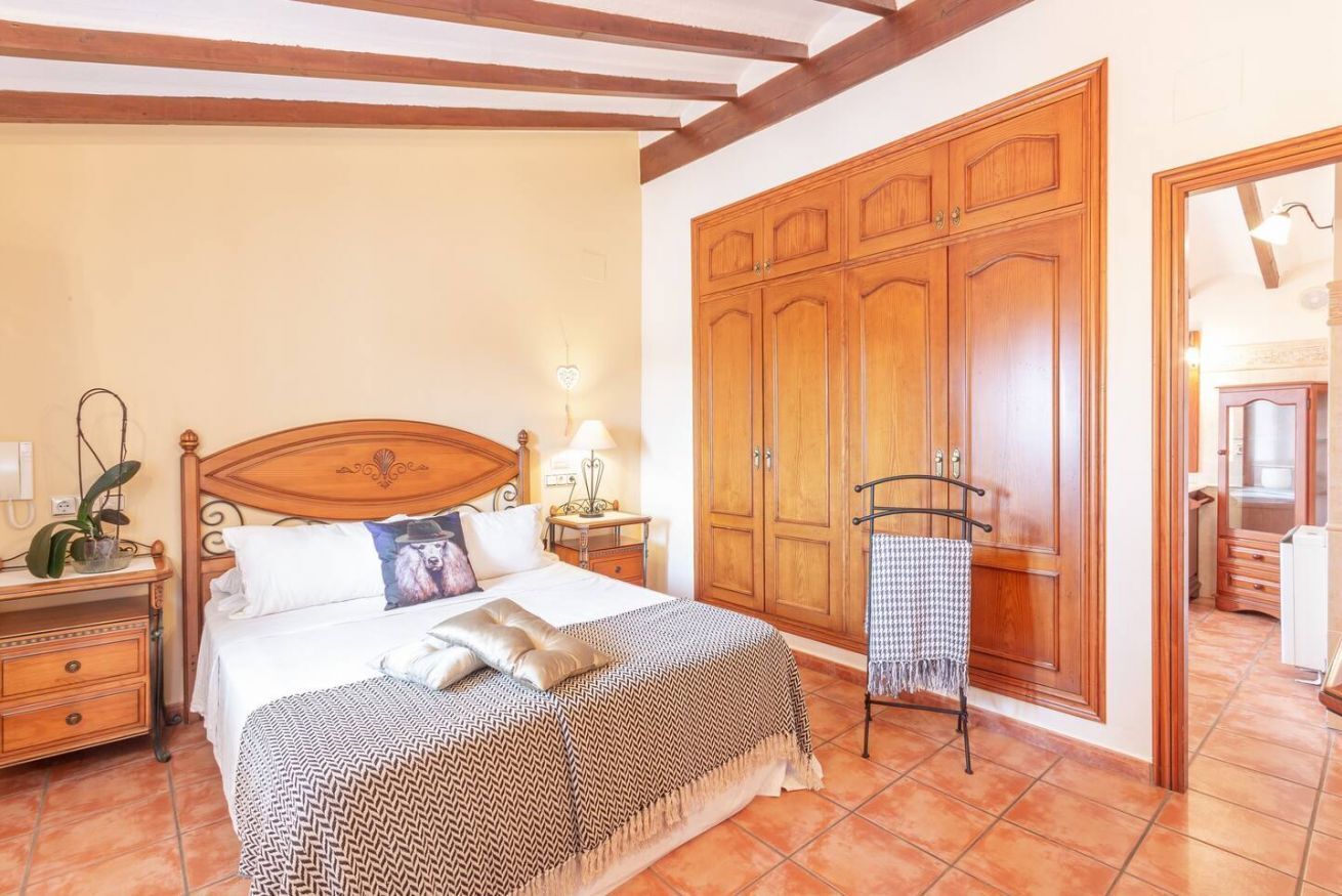 A bedroom with a wooden bed, a nightstand with a lamp, a wardrobe, and a mirror.