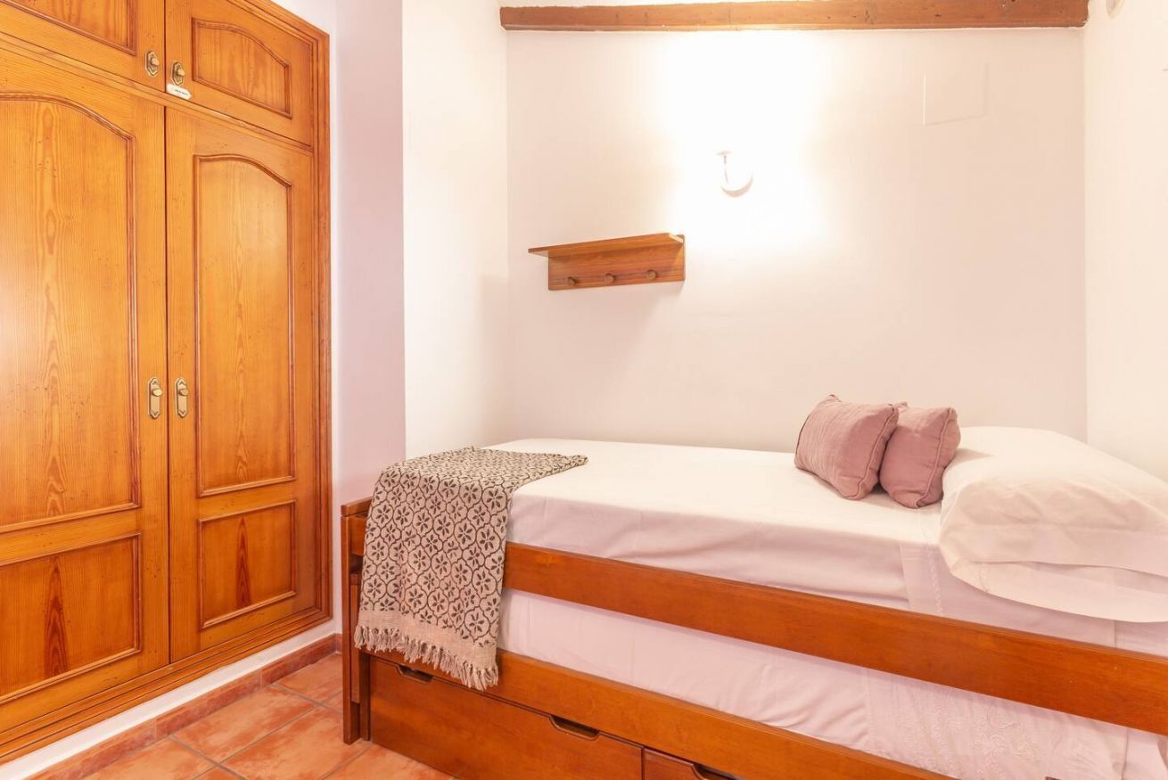 Un dormitorio con una cama de madera, una mesita de noche, un armario y un estante en la pared.