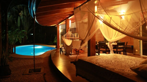 A bedroom with a bed, a mosquito net, a small pool, and a dining area with chairs and a table.