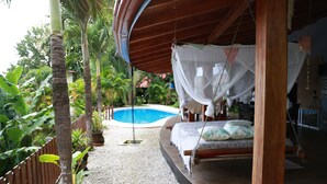 A bed with a canopy, a hanging swing, and a pool in the background.