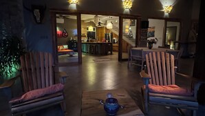 A cozy living room with wooden chairs and a coffee table, a kitchen in the background, and a ceiling fan.