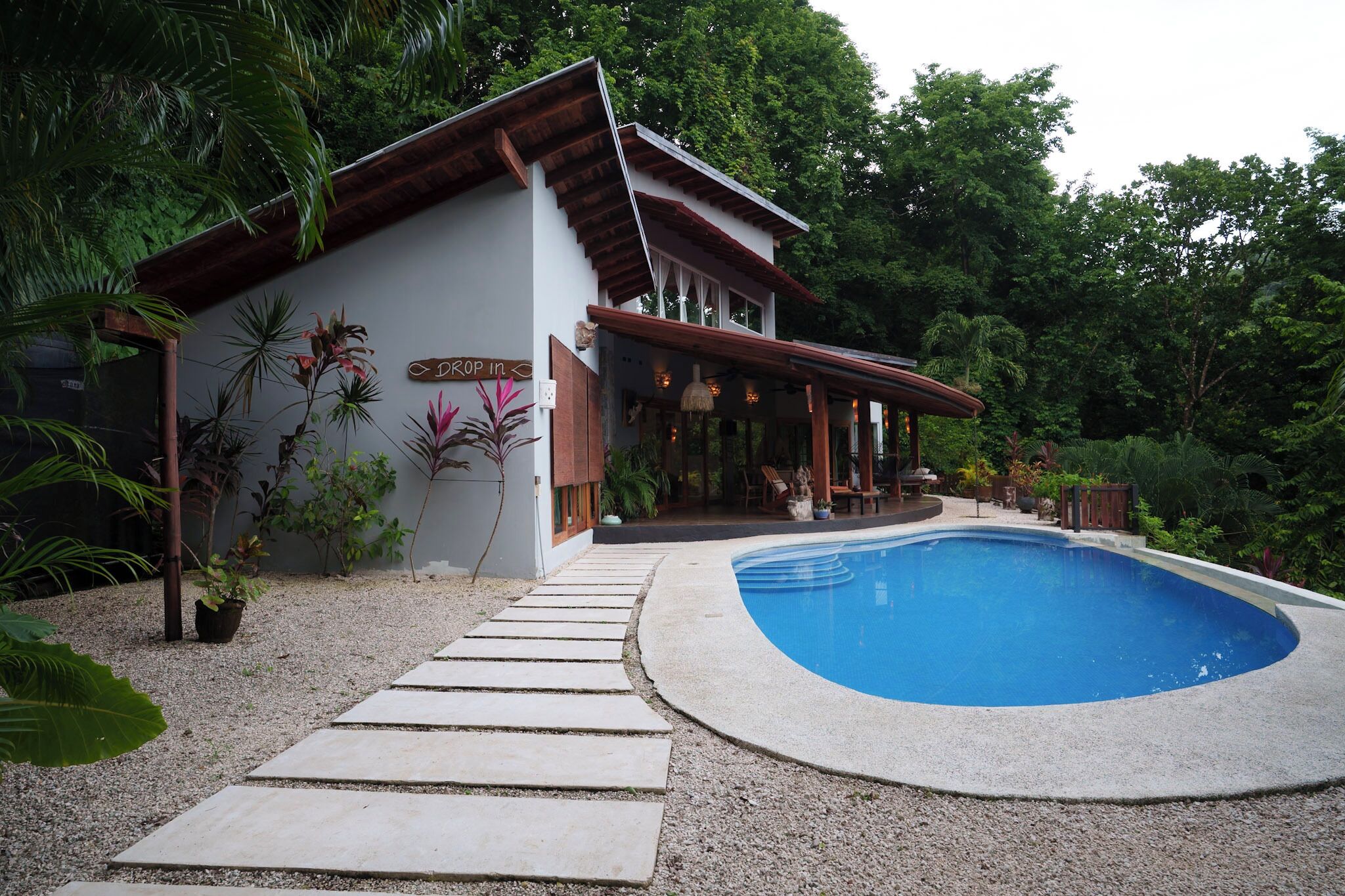 A house with a swimming pool, surrounded by greenery and a stone pathway.