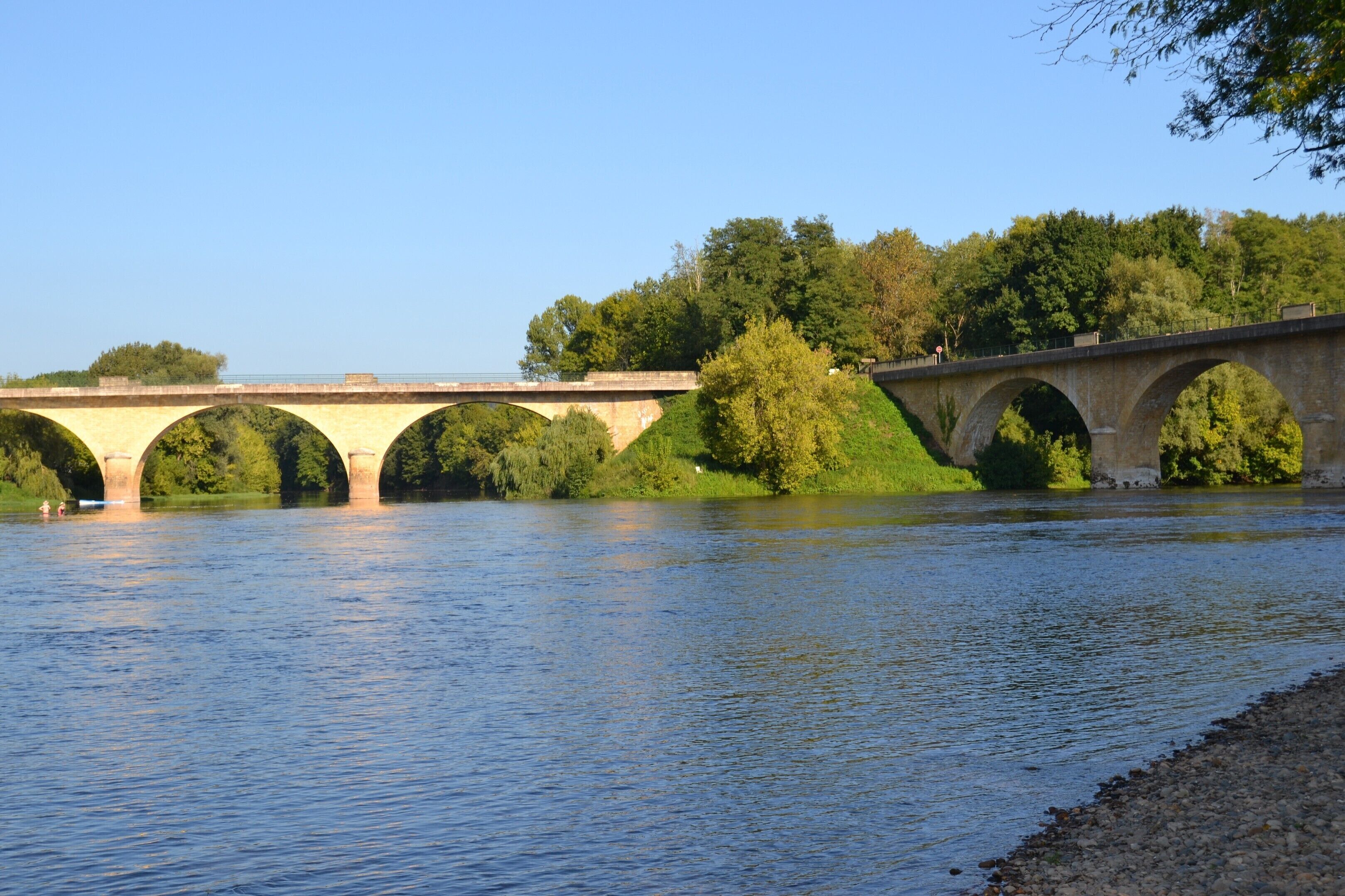 A stone bridge over a river with greenery on both sides.