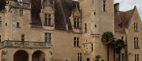 Un bâtiment historique en pierre, doté d’une tour centrale, d’une entrée en arc de cercle et d’une façade symétrique.