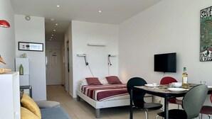 Ein moderner, gut beleuchteter Raum mit einem Bett, einem Esstisch mit Stühlen, einem Fernseher und einem Bild an der Wand.