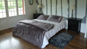 A bedroom with a large bed, two bedside tables with lamps, a mirror, and a view through a door. - ---- The cottage --- (ST LEGER DE ROTES)