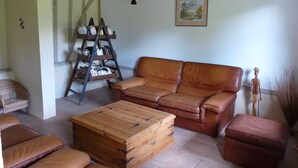 A living room with a brown leather sofa, a wooden chest, and a ladder bookshelf. - ---- The cottage --- (ST LEGER DE ROTES)
