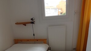 Ein kleines, sauberes Zimmer mit zwei Einzelbetten, einem Holzkopfende, einem Fenster mit Blick auf Gebäude und einer Heizung.