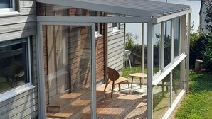 Una veranda moderna interamente in vetro con un pavimento in legno, un tavolo e una sedia.
