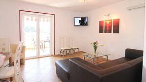 A modern living room with a sofa, a glass coffee table, and a TV mounted on the wall. There are two chairs and a table with a vase of flowers. - With sea view in Apartment Bernstein in Porec. (Porec)