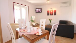 A dining area with a wooden table set for two, white chairs, and a television mounted on the wall. - With sea view in Apartment Bernstein in Porec. (Porec)