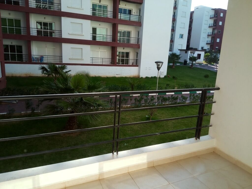 A balcony with a metal railing overlooking a grassy area and a building with multiple windows and balconies.