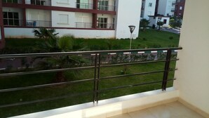 A balcony with a metal railing overlooking a grassy area and a building with multiple windows and balconies.