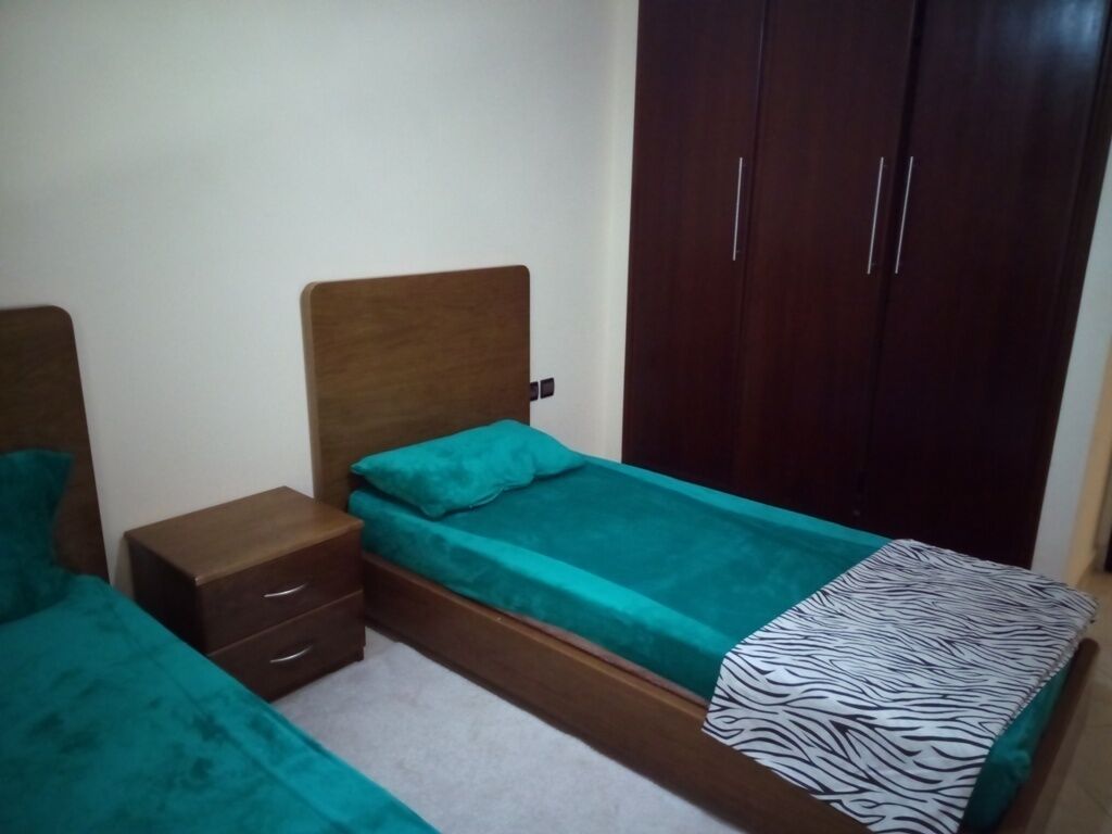 A bedroom with two single beds, a wooden wardrobe, and a nightstand with drawers.