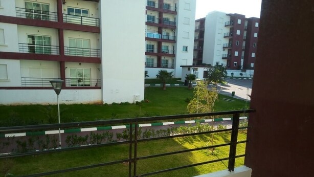 A balcony with a view of a green lawn and a multi-story building with balconies.