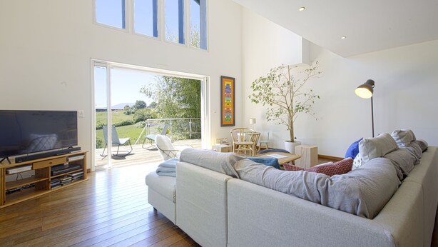 A modern living room with a large sofa, a TV, and a wooden entertainment unit. There is a sliding glass door leading to an outdoor area with a patio chair and a table. - House w/ pool - 12 pers., quiet garden w/ stunning view on the BASQUE COUNTRY (ARCANGUES)