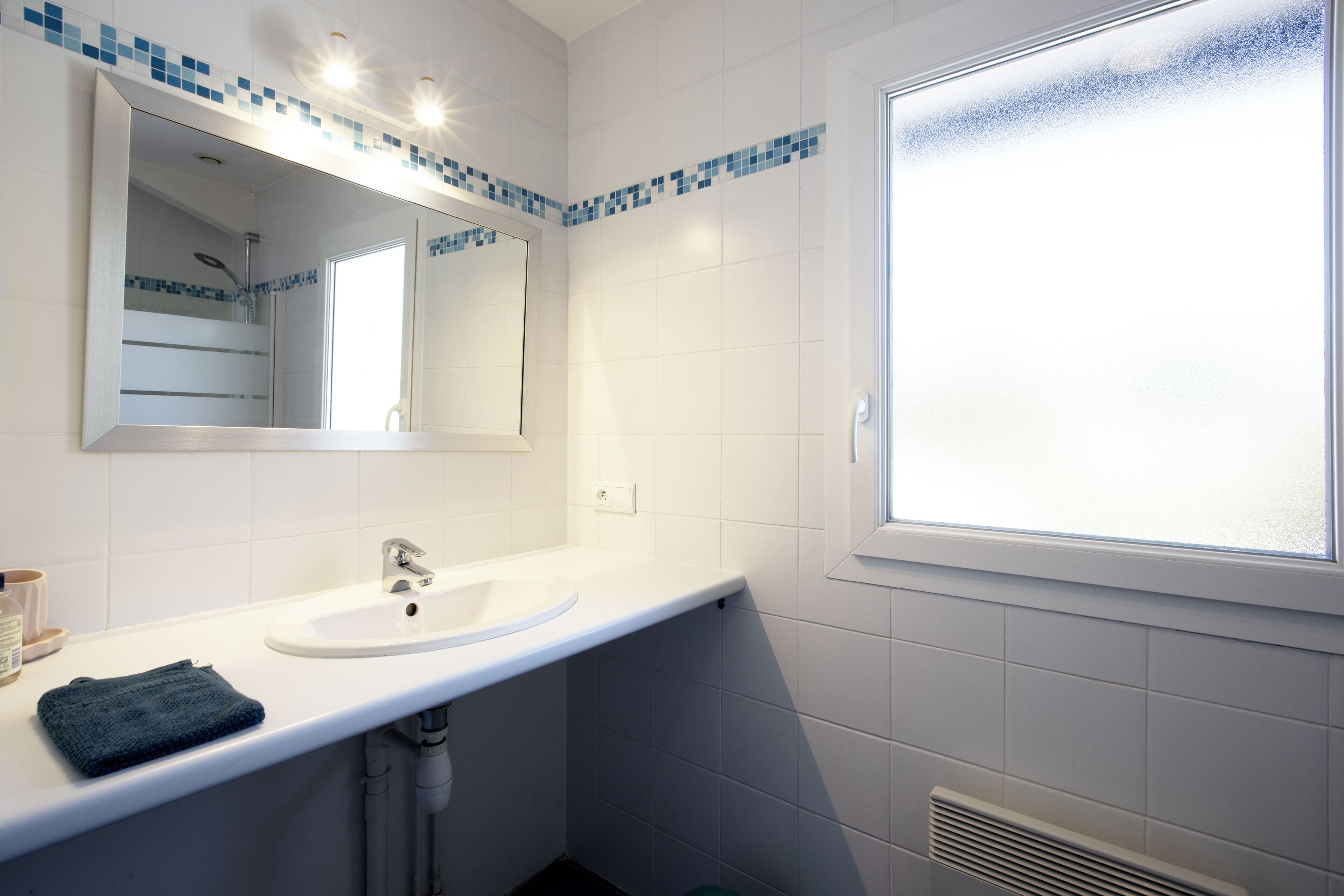 Ein Badezimmer mit weißem Waschbecken, Spiegel und Fenster.