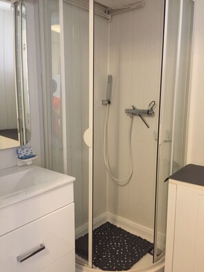 Une douche avec une porte en verre, un lavabo blanc et un tapis noir sur le sol.