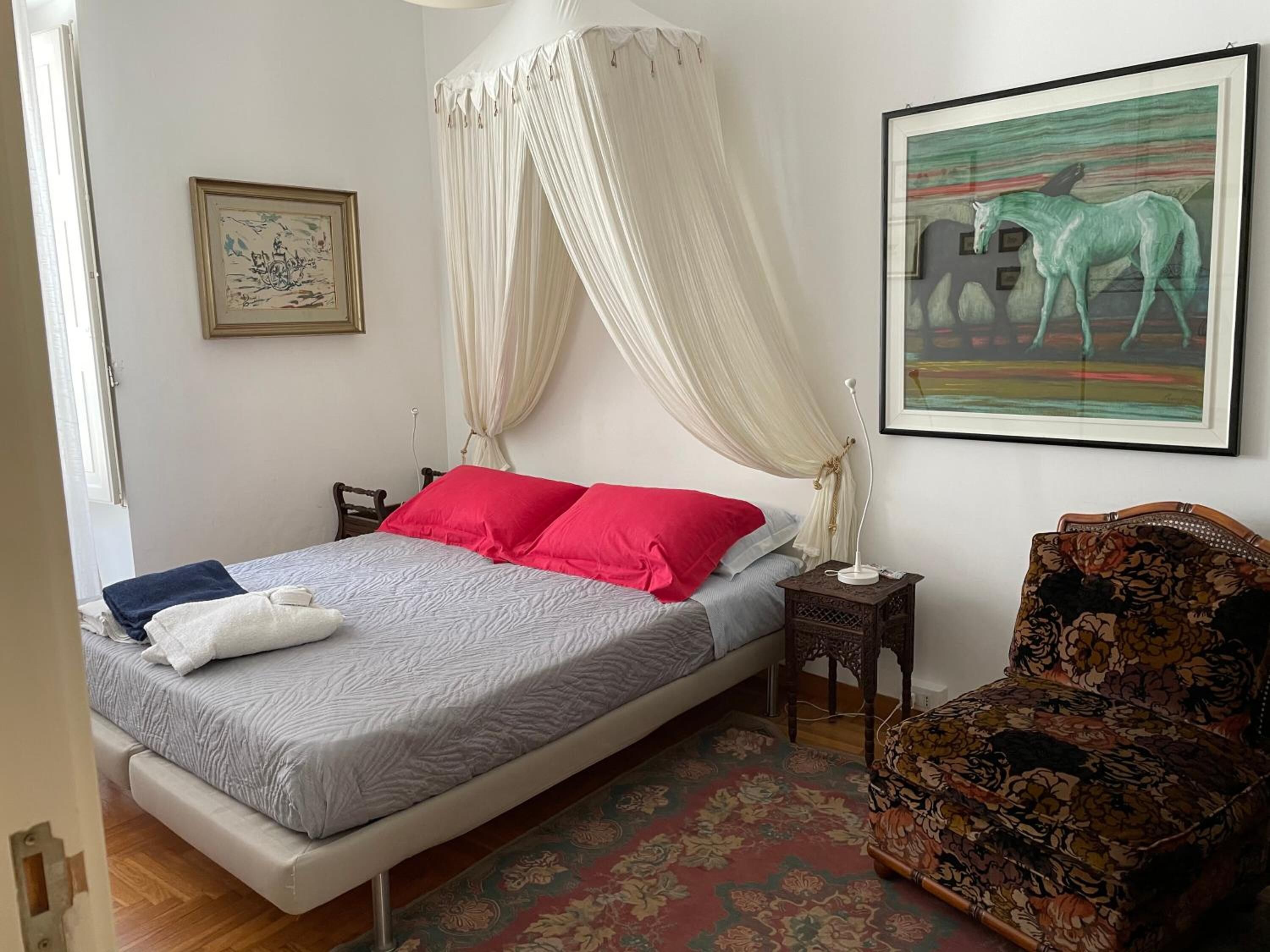 A bedroom with a bed, a nightstand, a chair, a canopy bed, a framed picture, and a rug.