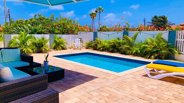 A swimming pool with a tiled edge, surrounded by a patio area with wicker furniture and a white fence. - Romantic, Beautiful Sunsets w/Private Pool (West Punt)