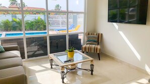 A living room with a glass coffee table, a striped armchair, a sofa, and a TV on the wall. - Romantic, Beautiful Sunsets w/Private Pool (West Punt)
