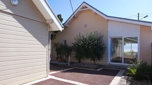 A residential building with a garage door, a covered patio, and a small garden area with potted plants. - Villa familiale avec chalet proche centre et plage (044) (Biscarrosse)