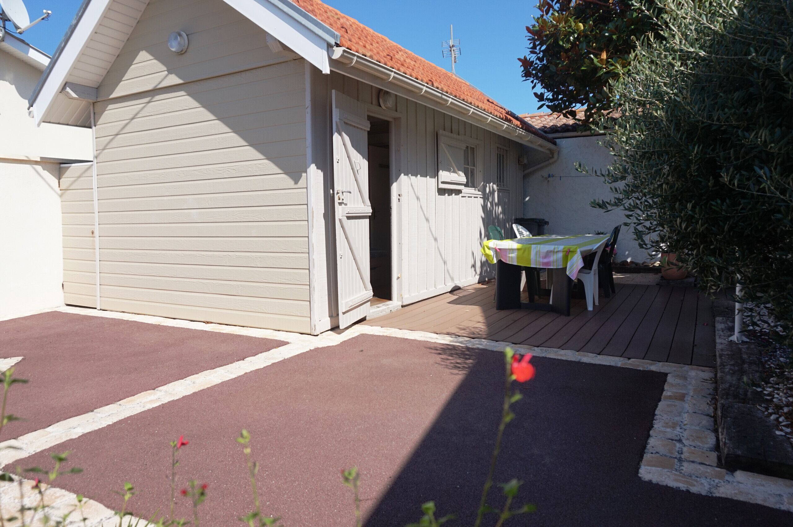 A small, single-story building with a red-tiled roof, a covered outdoor seating area, and a door leading to an interior space.