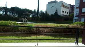 A balcony with a metal railing overlooking a grassy area with a bench and a small structure. - Atlantic Ocean Residence 1501 (Asilah)