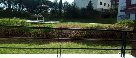 A balcony with a metal railing overlooking a grassy area with a bench and a small structure.