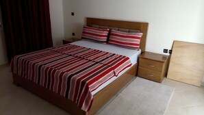 A bedroom with a wooden bed, striped bedding, a nightstand, and a wooden headboard. - Atlantic Ocean Residence 1501 (Asilah)
