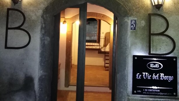 An entrance with two illuminated 'B' signs, an archway, and a signboard for 'Le Vie del Borge' with contact information. - B&B Le Vie del Borgo (Castiglione di Sicilia)