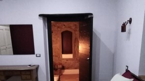 A bedroom with a bed, a desk, and a mirror. There is a door leading to a bathroom. - B&B Le Vie del Borgo (Castiglione di Sicilia)